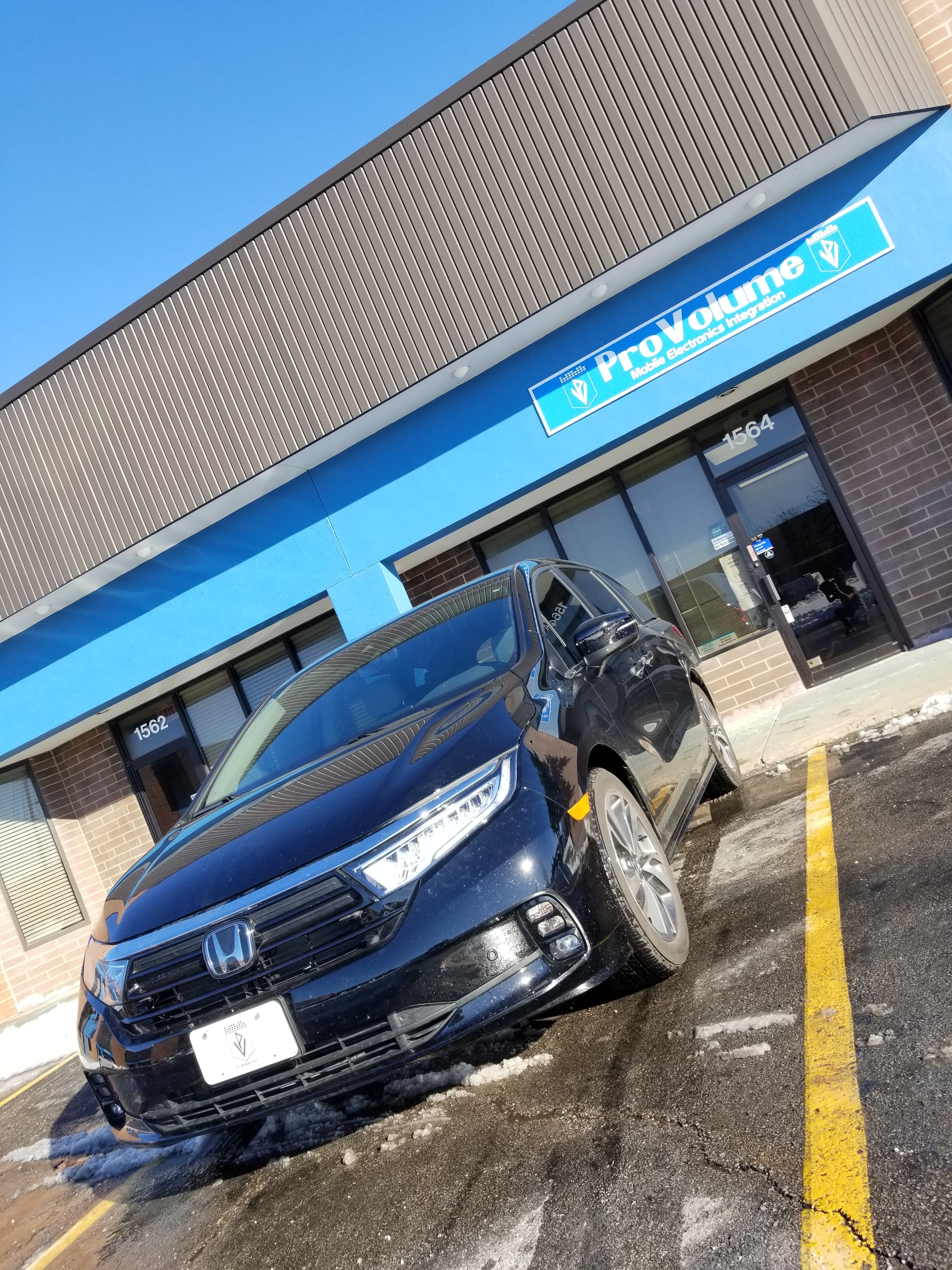 Black Honda Odyssey parked in a lot outside a ProVolume Mobile Electronics Integration storefront.